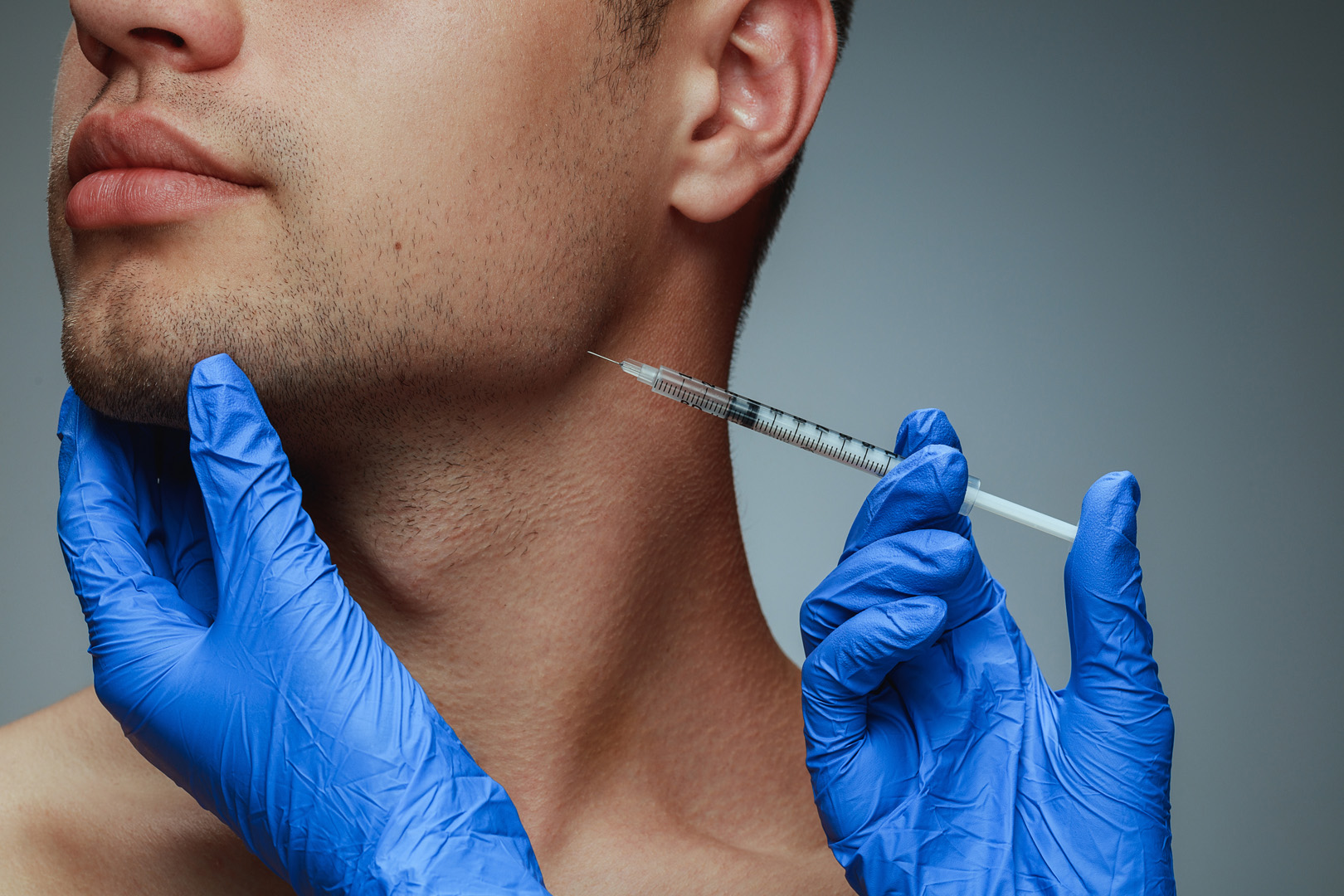 A gloved clinician injecting along a man's jawline