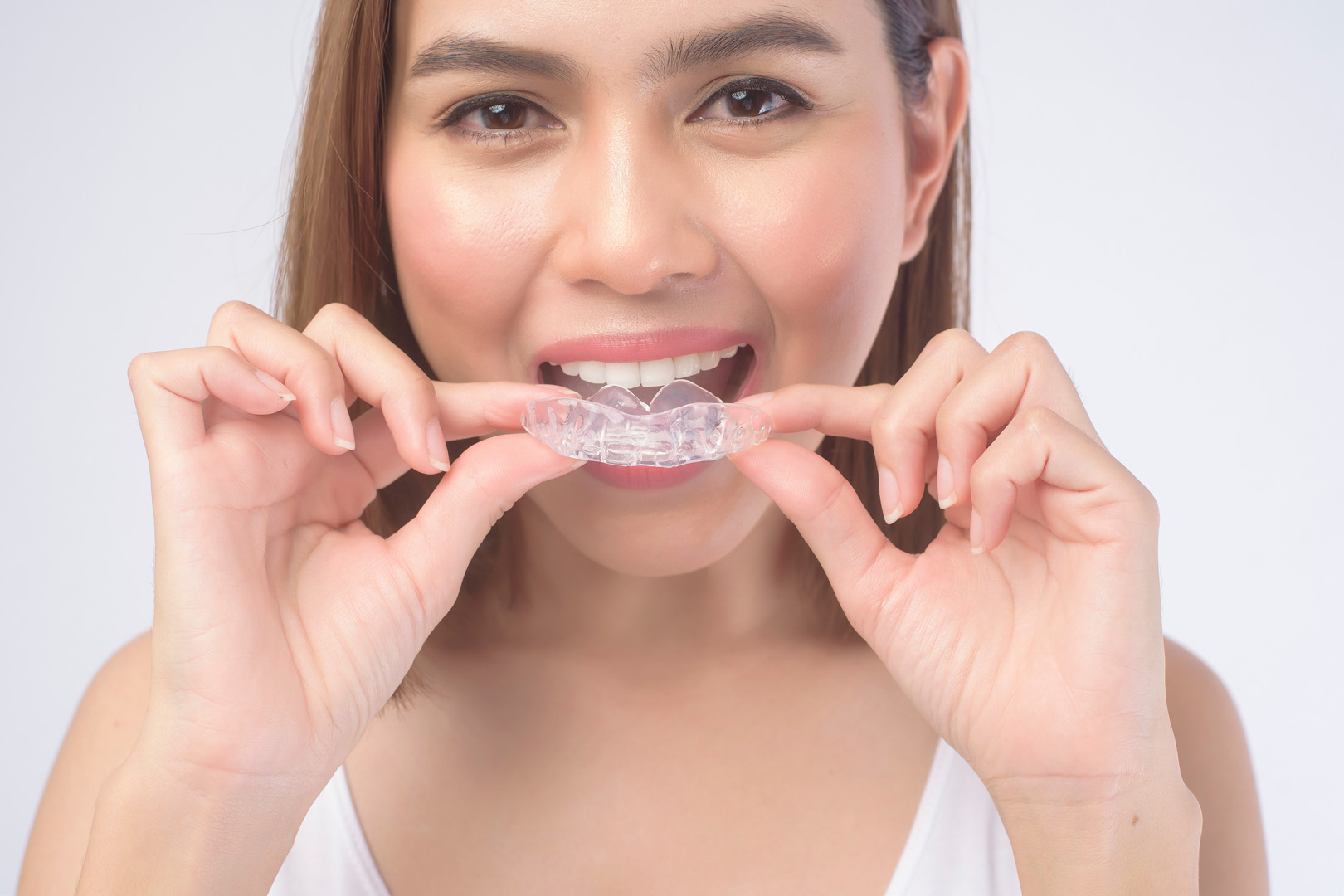 A woman holding a clear mouthguard up to her teeth