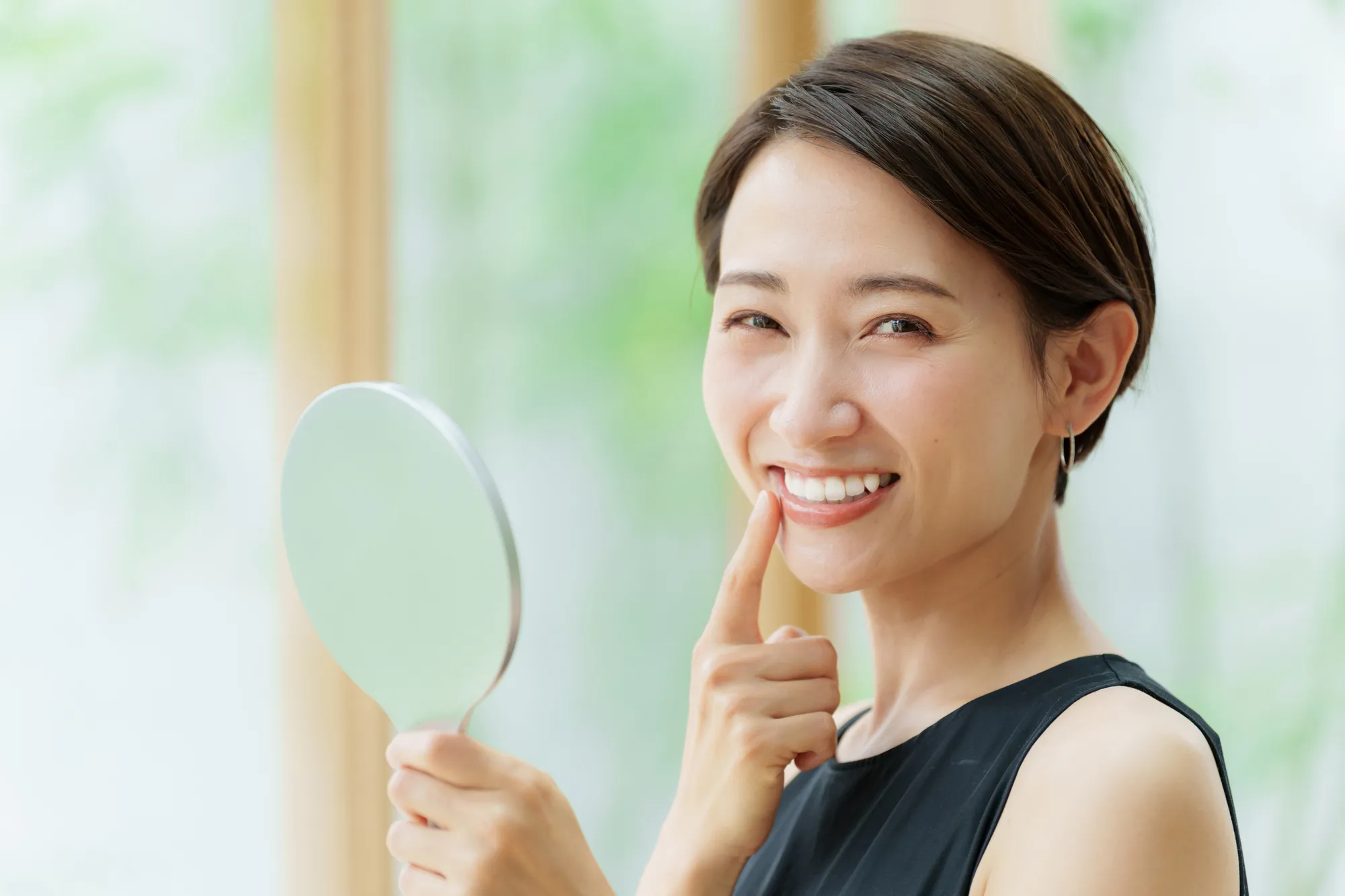 A woman holding a hand mirror and pointing at her smile