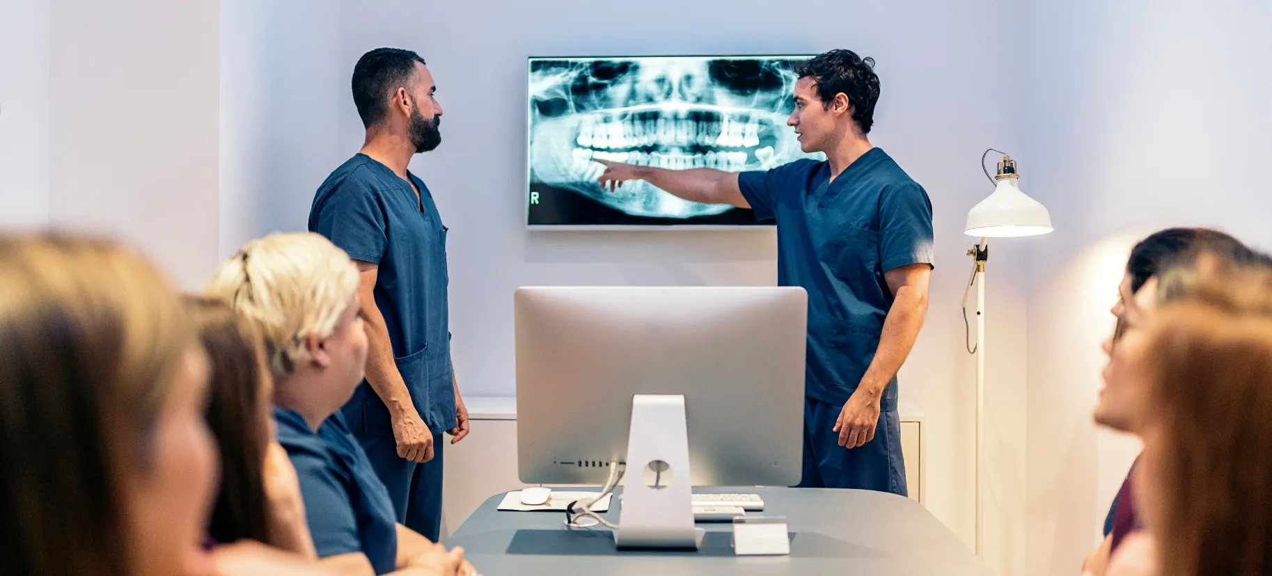 Clinical staff gathered as a dentist points to a panoramic X-ray on a wall-mounted screen