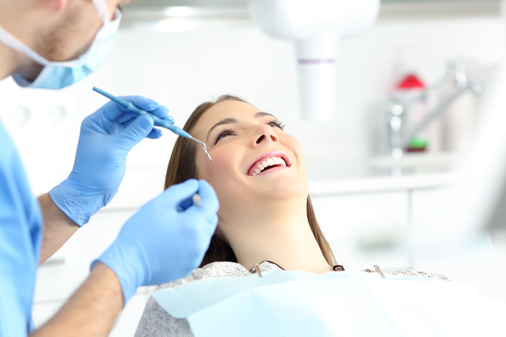 A patient smiling in the chair as a dentist reaches in to work on her front teeth