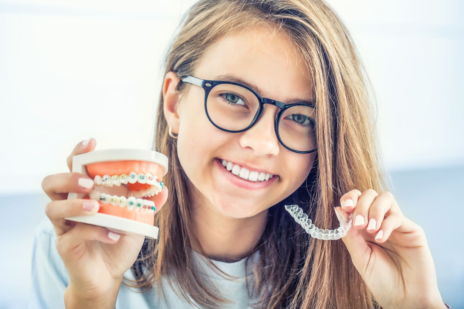 A girl holding a model of braces in one hand and a clear aligner in the other
