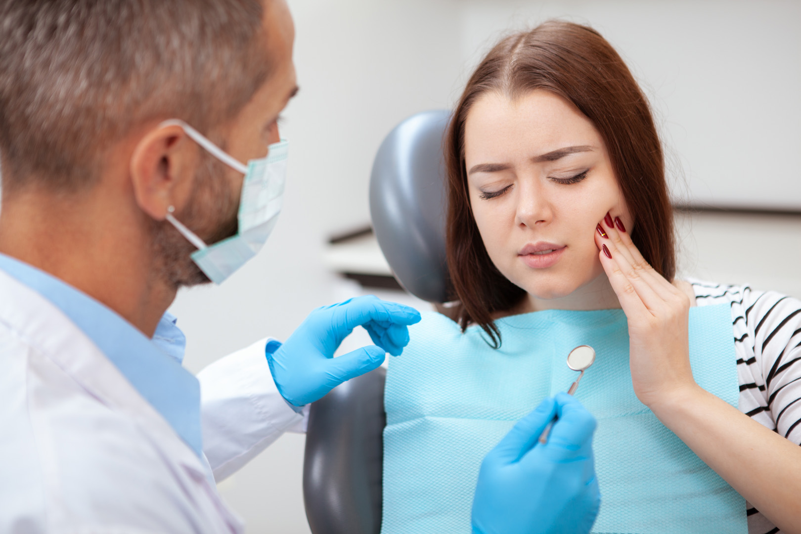 A patient holding her cheek in pain while a dentist examines her